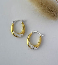 Load image into Gallery viewer, A pair of gold and sterling silver two tone oval shaped hoop earrings with a textured silver band