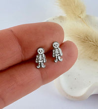 Load image into Gallery viewer, Small skeleton earrings held between fingers with a neutral background