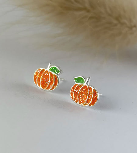 close up of sterling silver pumpkin stud earrings that are orange with glitter and a tiny green leaf