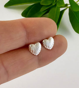 Silver heart shell-shaped earrings held between fingers