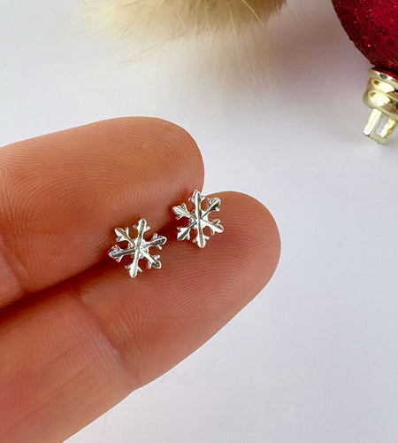 Silver snowflake earrings held between fingers against a white background