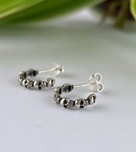 Load image into Gallery viewer, A pair of small silver hoop earrings with a row of tiny sterling silver skulls. 