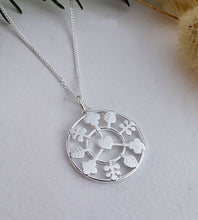 Load image into Gallery viewer, Silver necklace with a circular pendant featuring heart and leaf designs on a light gray background.