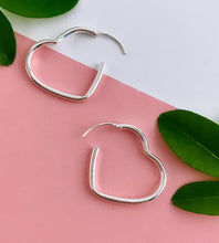 Load image into Gallery viewer, sterling silver heart hoops open to show how to pull apart and put the thin post through your ear to wear