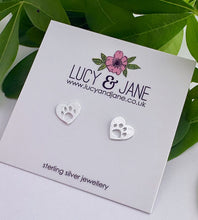 Load image into Gallery viewer, sterling silver heart studs with a paw print cut out. Displayed on a Lucy and Jane backing card
