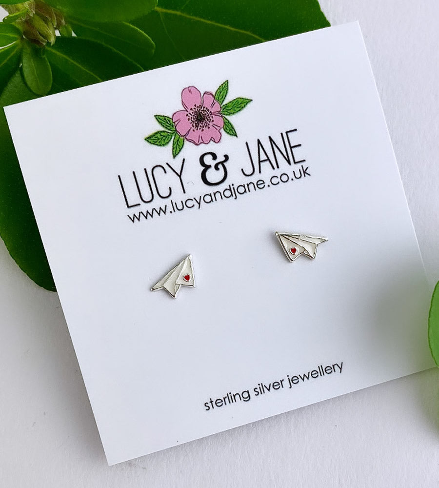 tiny white paper plane earrings with a little red heart on the wing