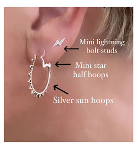 trio of sterling silver earrings in model's ear - mini silver lighting bolt studs, mini silver star hoops and sterling silver sun hoops